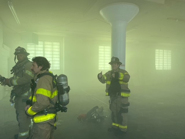 Firefighters stand in open room with smoke in the air