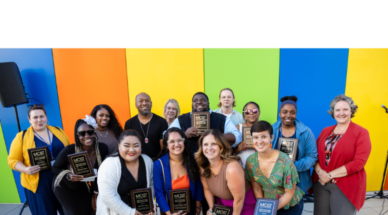 Image of group with the Mayor holding plaques in front of rainbow-colored background