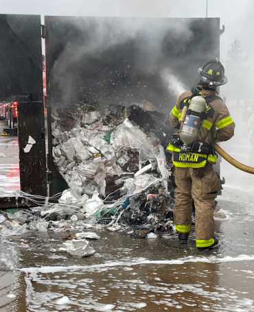 Firefighters sprays water on to heaps of trash inside compactor