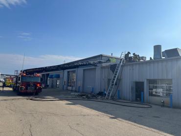 Ladder 6 with aerial ladder extended and firefighters on the roof of auto repair shop