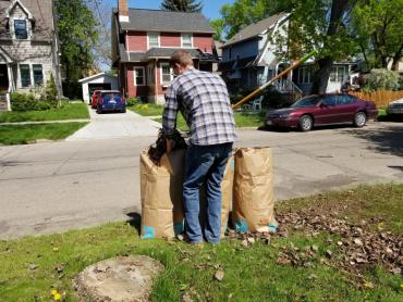 A tall mysterious man stuffing leaves into compostable paper leaf bags that are waiting for pickup