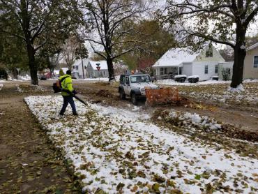 Leaf collection in the snow. Blowing leaves so they can be pushed into a truck.