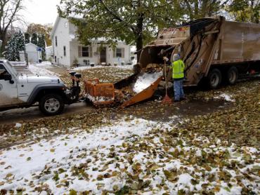 Leaf collection in the snow. Pushing leaves into a rear-loading truck.