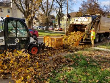 Photo from 2019 of leaf collection crews pushing leaves into a truck.