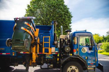 This is a City of Madison collection truck lifting and dumping a green recycling cart into the top of the blue collection vehicle.
