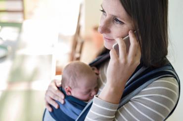 A person talking on a cell phone with a baby in a sling on their chest