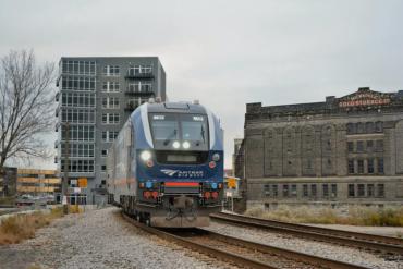 Image of blue and gray Amtrak train in city setting. 