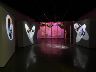 Image of multicolored abstract projection installations in a dark, large, white room. 