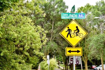 圖片顯示了一個菱形黃色標誌，上面有一個行走的圖形和一個騎自行車的圖形。 上面是一個綠色的路牌，上面寫著“自行車道”