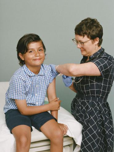 a child, seated, getting vaccinated by a woman, standing