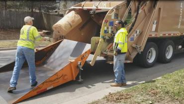 Bagged yard waste being tossed into a collection truck