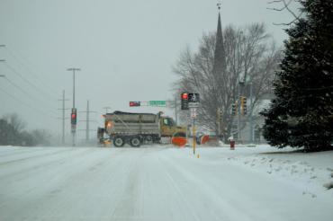 This is an older photo of a City of Madison plow truck driving through an intersection.