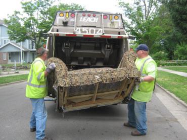 Two Streets Division employees loading a couch into a rear-loading garbage truck