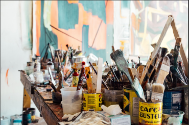 Paint brushes in coffee cans on a table with a mural in the background