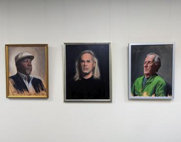 Three realistic paintings of men sit side by side on a white wall.