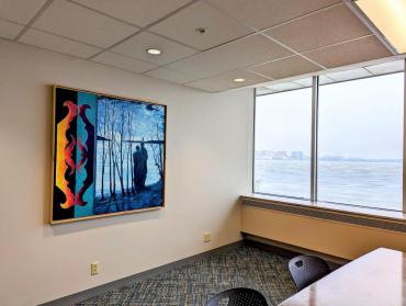 An image of  colorful painting on a wall near windows looking out to a lake.