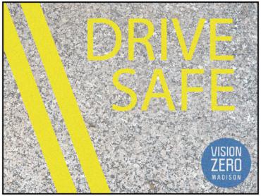 Imagen de una carretera con marcas de líneas amarillas que dicen "Conduce con seguridad" con el logotipo redondo de Vision Zero