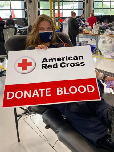 Firefighter Seeber holds a sign saying "Donate Blood" while giving blood in 2020