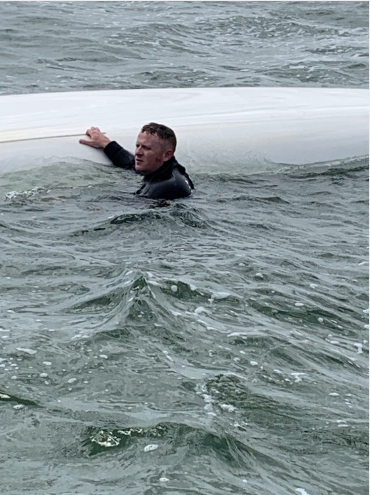 Rescuer in water next to capsized boat