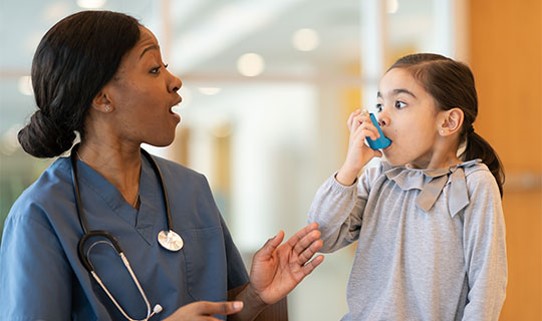 A nurse helps a child use an inhaler.