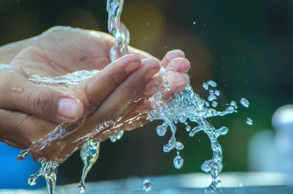 A person catches water from a fountain in their cupped hands .