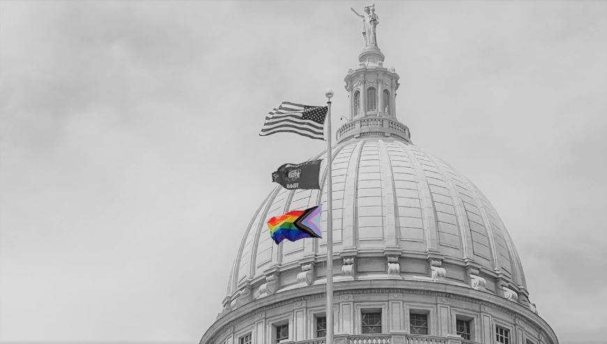 Event Header Image features the State of Wisconsin Capitol building dome and Lady Forward. In front of this is a flagpole with the flag of the United States, the State of Wisconsin flag, and the LGBTQ+ Flag waving in the wind. All but the LGBTQ+ flag is in black and white.