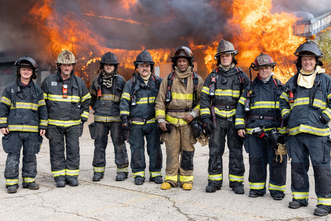 Madison College instructors posing in front of the building burning behind them