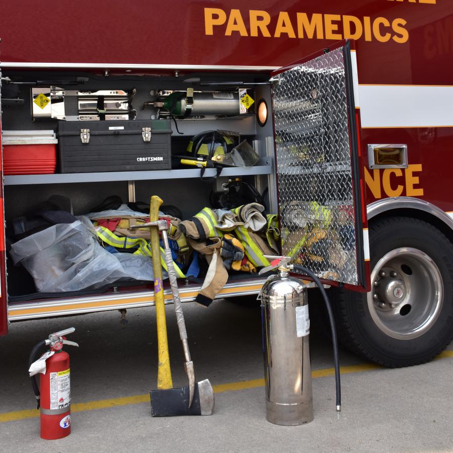 Extinguisher, axe, halligan, and water can next to ambulance