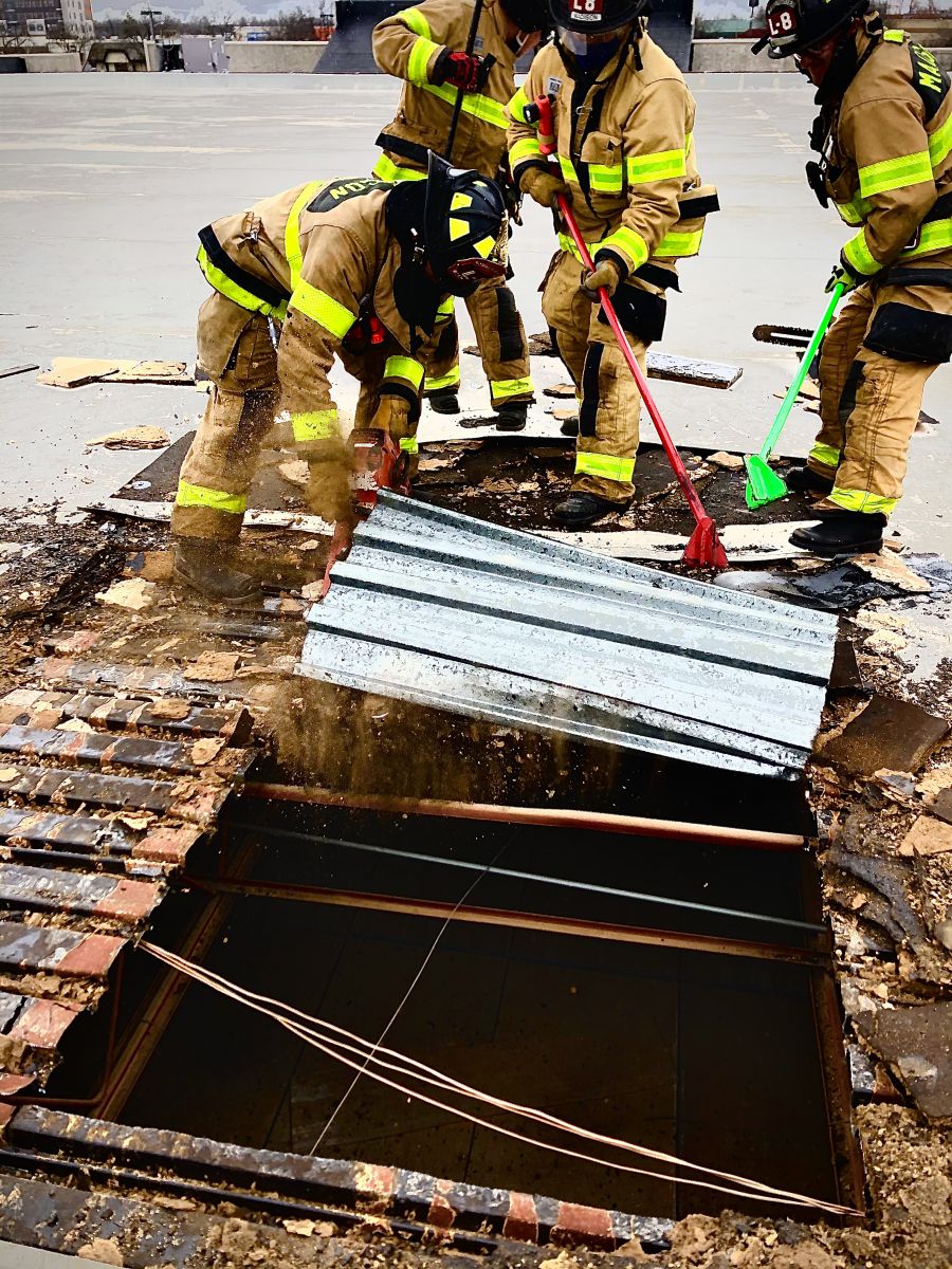 firefighters peel back corrugated metal on rooftop