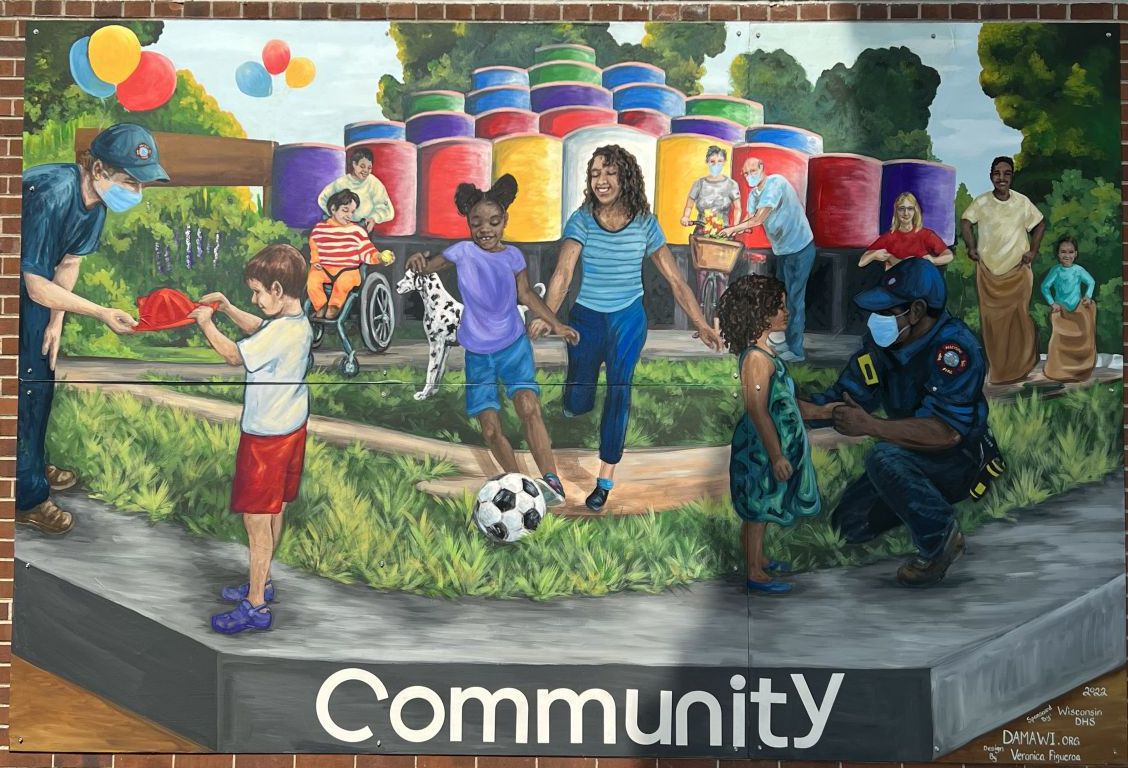 The mural depicts two masked Madison firefighters interacting with children, with the word "Community" across the bottom