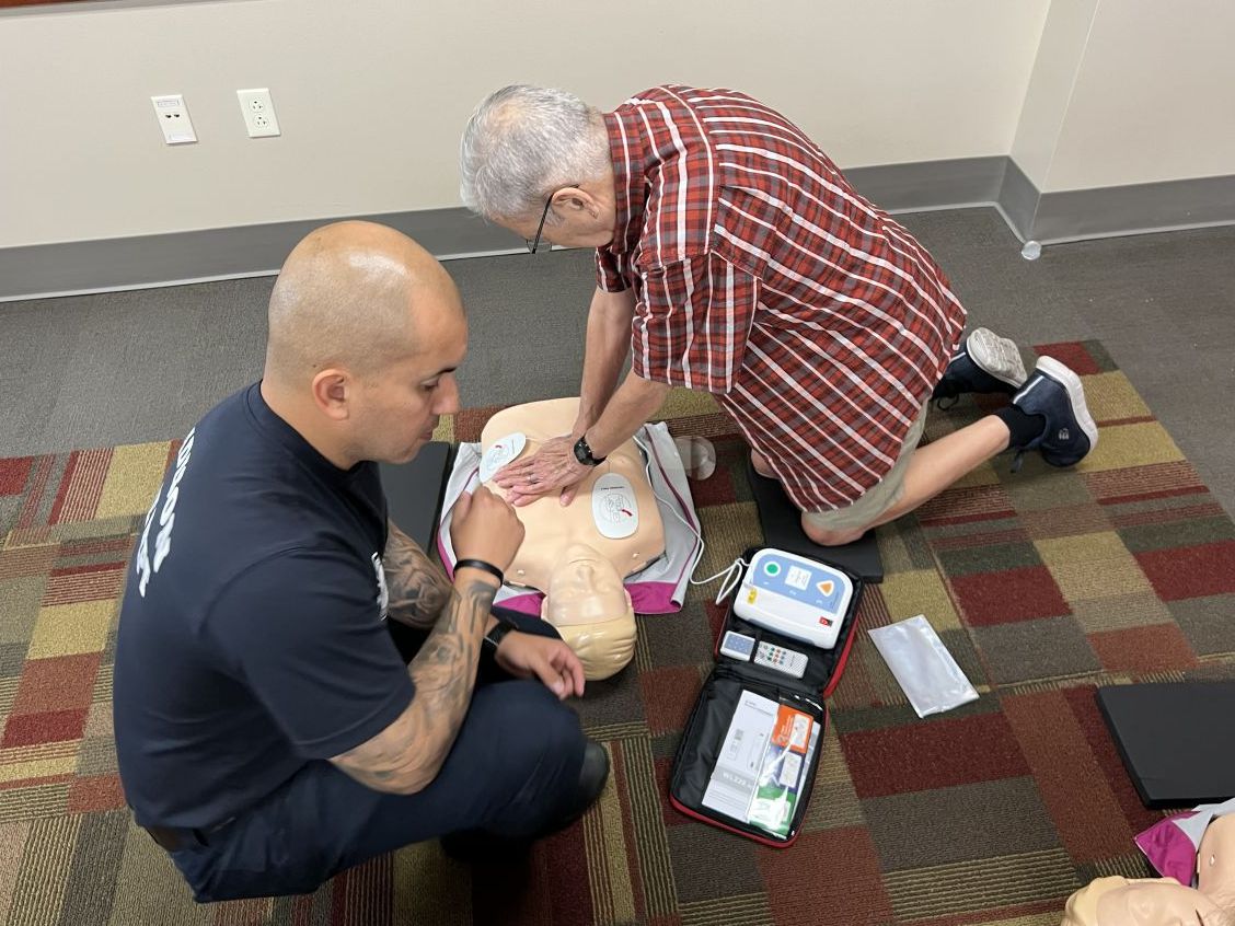 A community member performs hands-only CPR on a training manikin with an EMT supervising