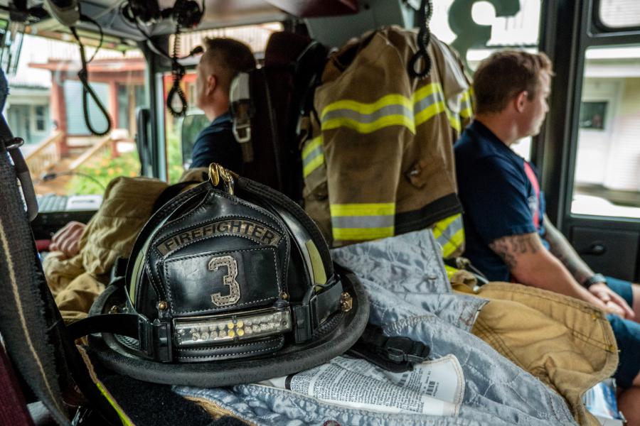 Two firefighters sitting in a truck. A helmet with "Firefighter Station 3" is sitting in the foreground.