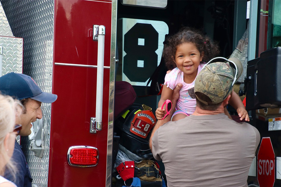 A smiling young child is lifted inside a fire engine on display