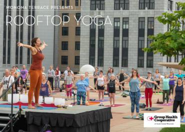 yoga instructor on outdoor rooftop stage surrounded by people doing yoga 