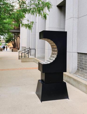 A stainless steel sculpture in the shape of an arc with a black exterior and a silver faceted interior.