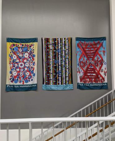 Vertical fabric flags with bright colors that say  Paa tsa numunaina (Water is Life in Comanche), by artist John Hitchcock
