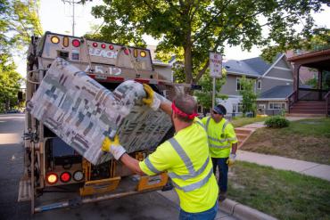 Two employees putting couch into garbage truck