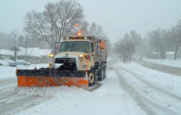 Plow truck pushing snow from the road during a snowstorm.