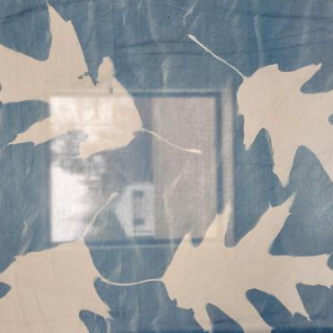 A detail photograph showing the white print left by an oak leaf on the blue cyanotype fabric that will be part of the public art installation, "Nature is Healing"
