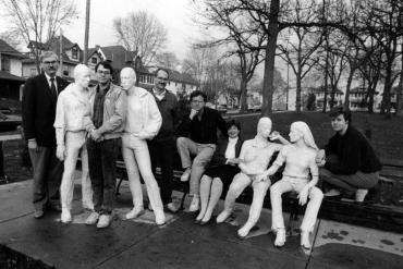 Black and white photograph of Dick Wagner and a group of other individuals standing with the white marble sculpture Gay Liberation by George Segal in Orton park. The sculpture features two men holding hands standing near two women who are sitting on a bench holding hands.