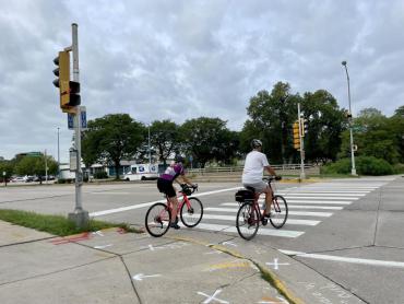 2 名自行車騎手在人行橫道的公園街十字路口過馬路的圖像。