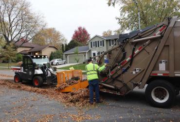 Crews pushing leaves into a rear-loading truck.