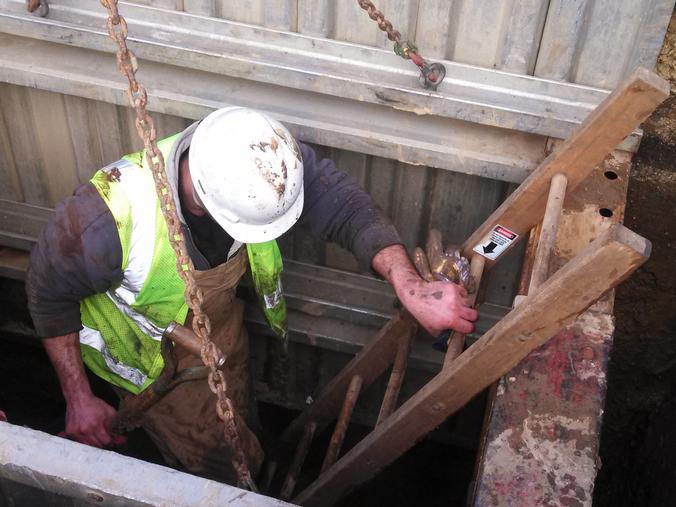 Worker climbs frm muddy pit after repairing main